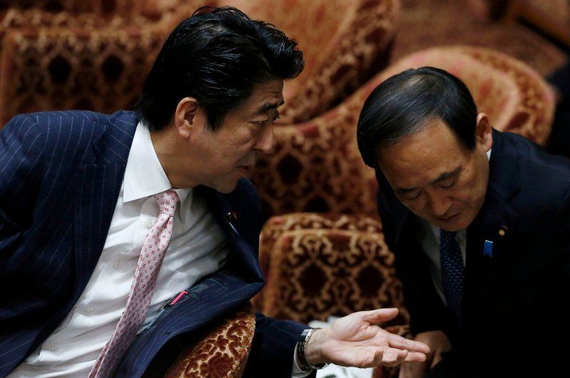 Yoshihide Suga having a conversation with Shinzo Abe