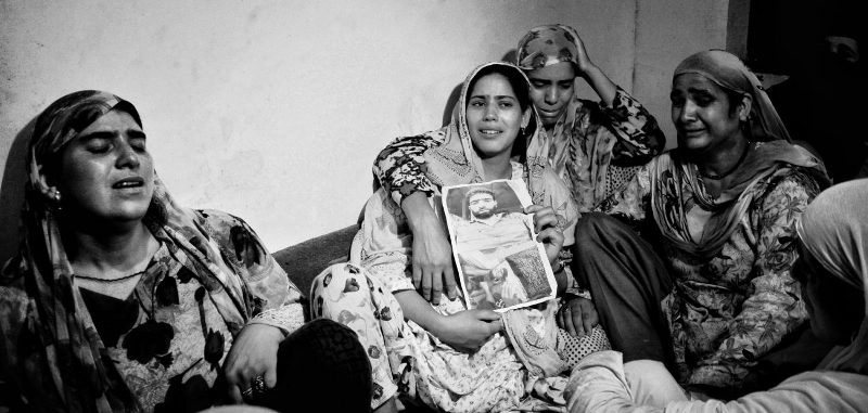 Firdous Ahman Khan's weeping wife, Ruksana (centre), with other women, holding a picture of her dead husband - image captured by Masrat Zahra