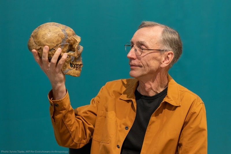Svante Pääbo posing for a photo with a Neanderthal's skull