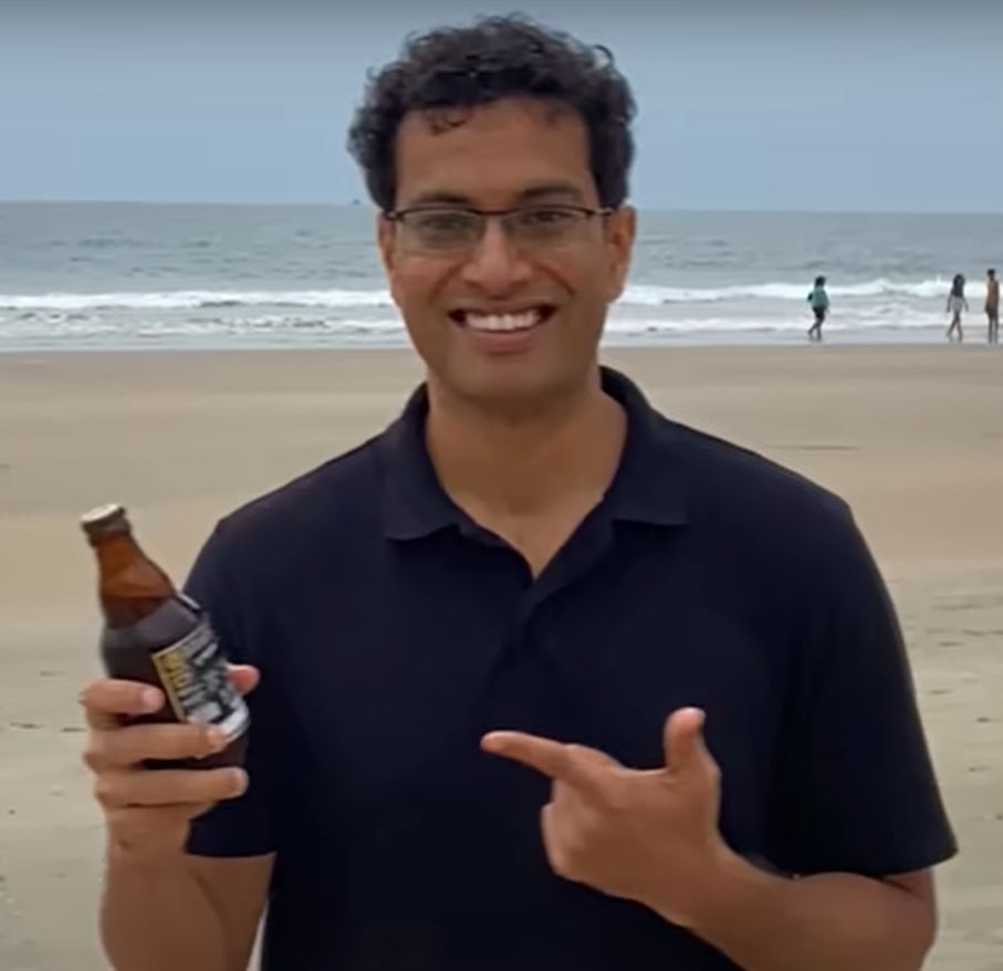 Akshat holding a bottle of beer on a beach in Goa