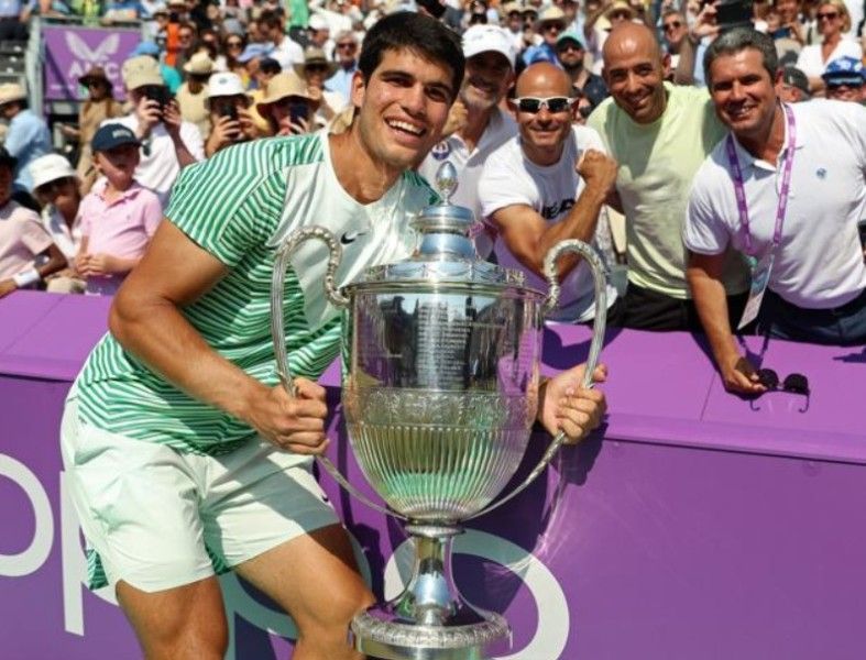 Carlos Alcaraz posing with a trophy with his father and support staff in the background