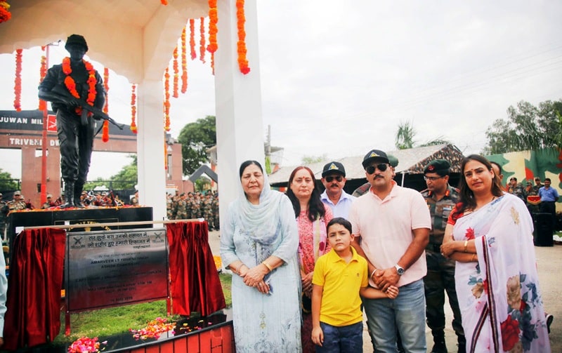 A photo of Triveni Singh's family standing next to his statue at the Sunjuwan Military Station