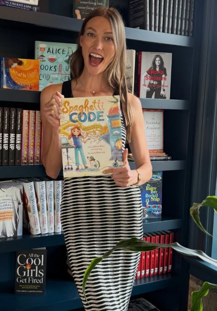 Karlie Kloss posing with her book, Spaghetti Code: A Story About Problem-Solving, Pasta, and the Power of Big Ideas